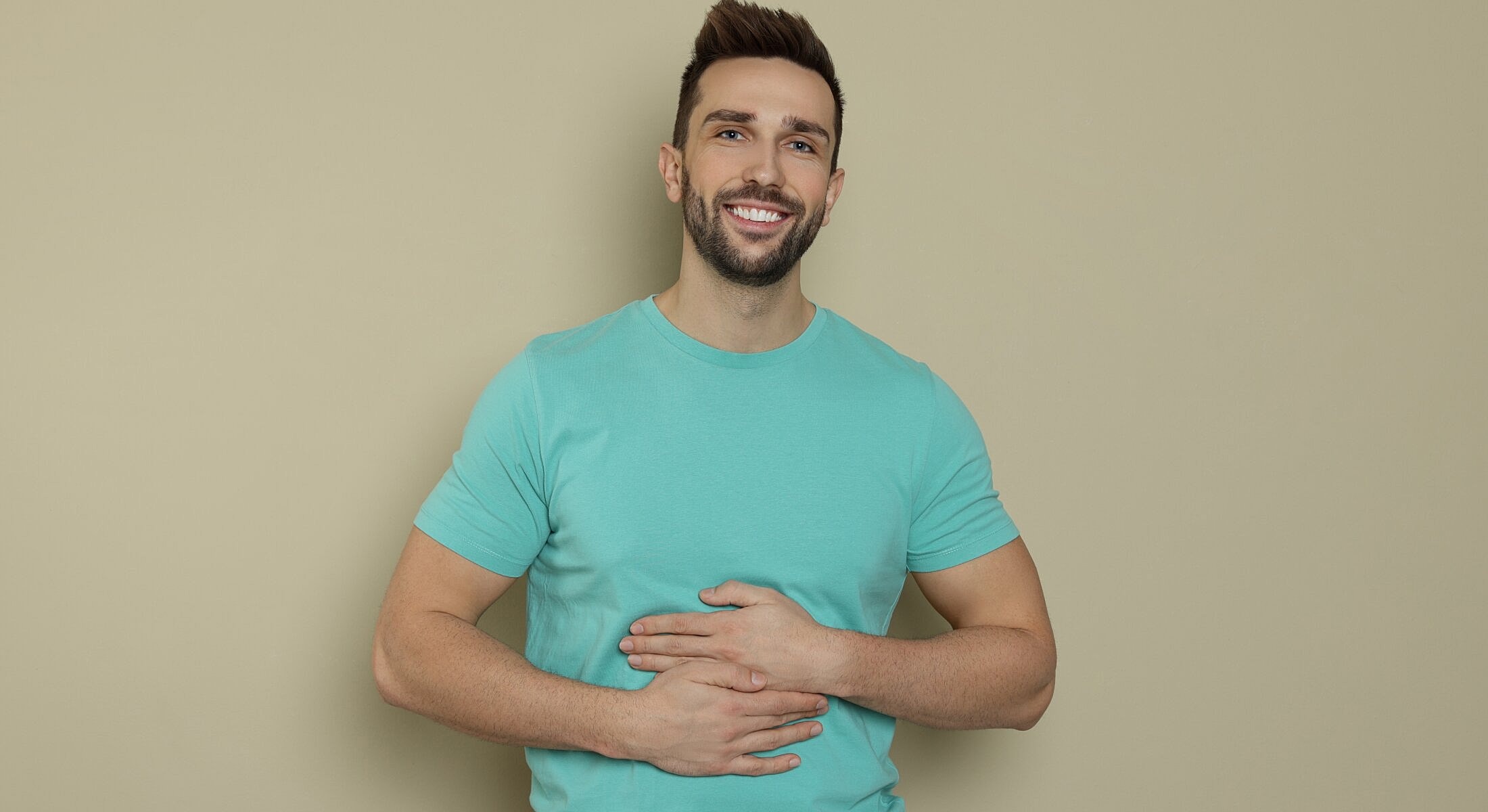 Smiling man in turquoise shirt against neutral background.