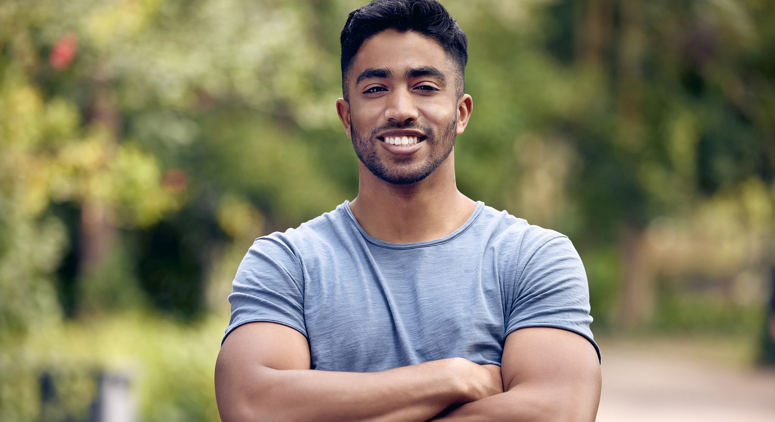 Smiling man with crossed arms outdoors.