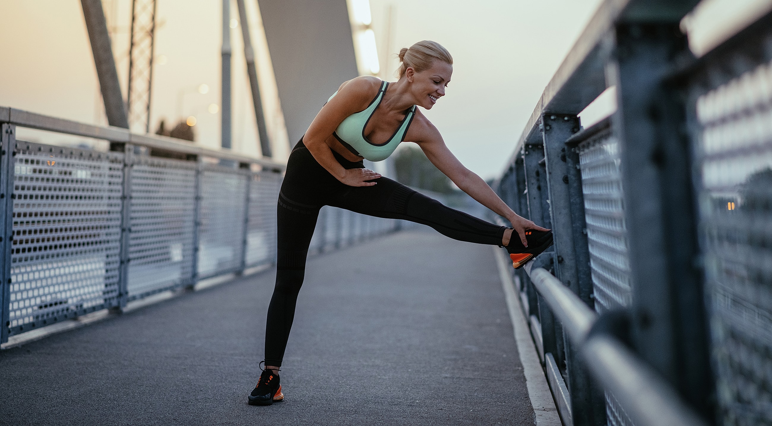 Woman stretching on a bridge at sunset.