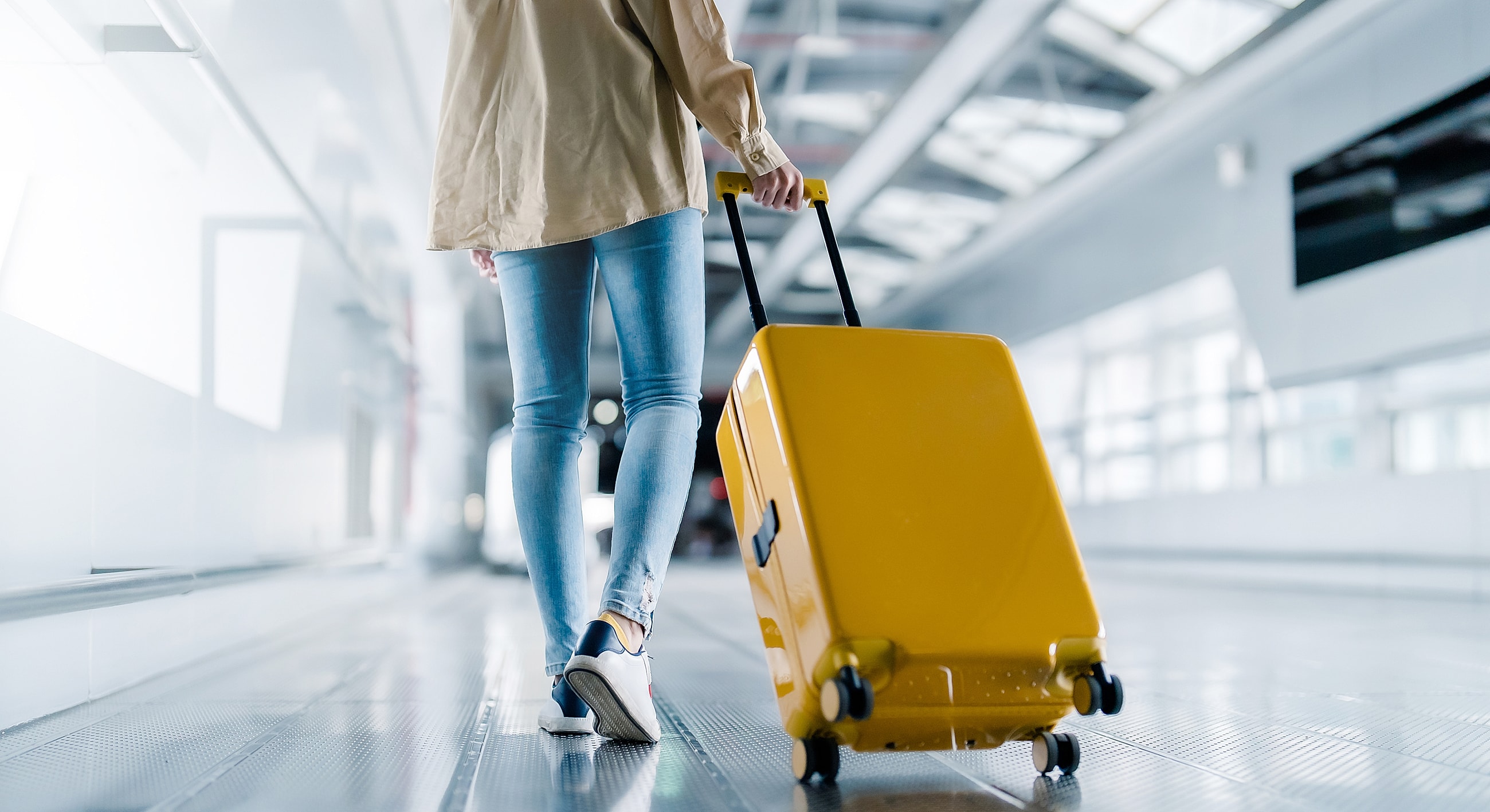 Person walking with a yellow suitcase indoors.